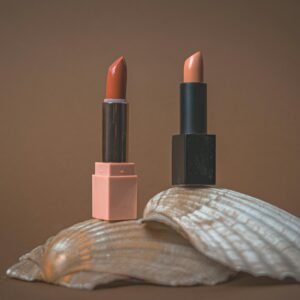 Two elegant lipsticks displayed on a seashell with a minimalist, earthy backdrop.